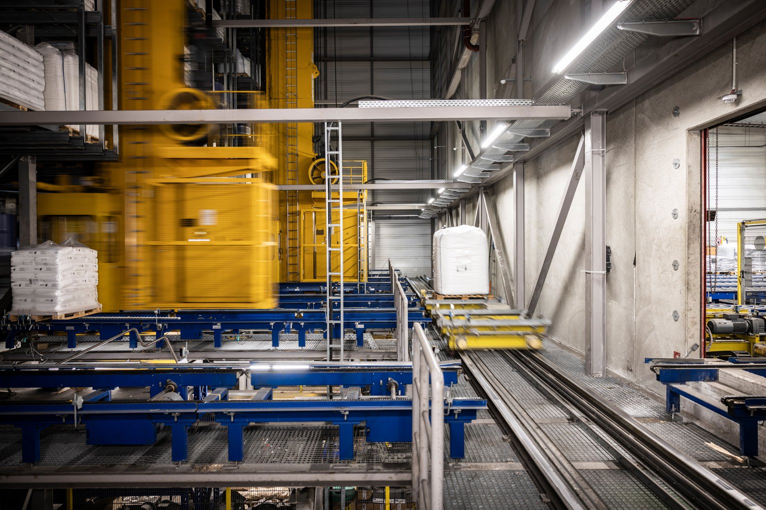 Fördertechnik im automatisierten Hochregallager Automatisiertes Fördersystem mit gelbem Regalbediengerät und Paletten in einem Hochregallager.