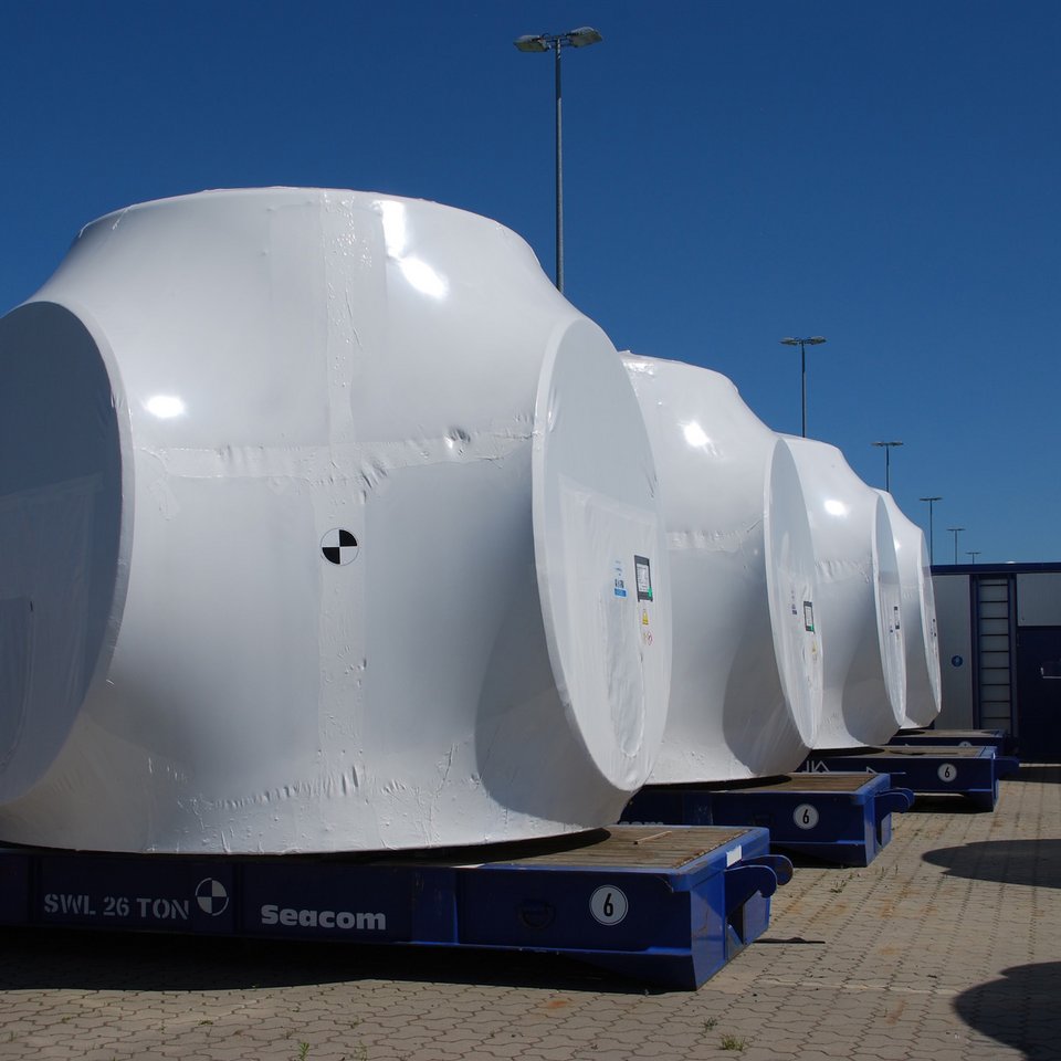 Nacellen von Windkraftanlagen in weißer Folie verpackt auf blauen Transportgestellen