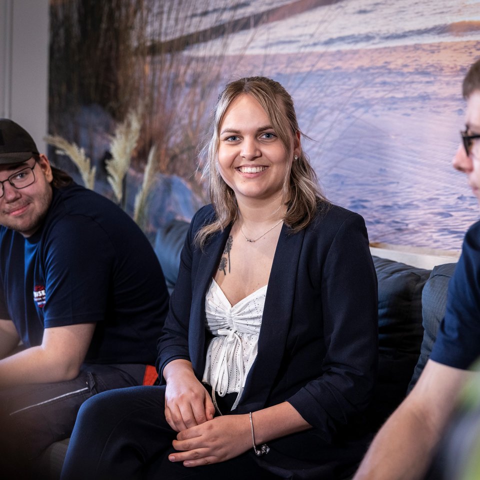 Drei Mitarbeitende sitzen lächelnd in einem Besprechungsraum und unterhalten sich.