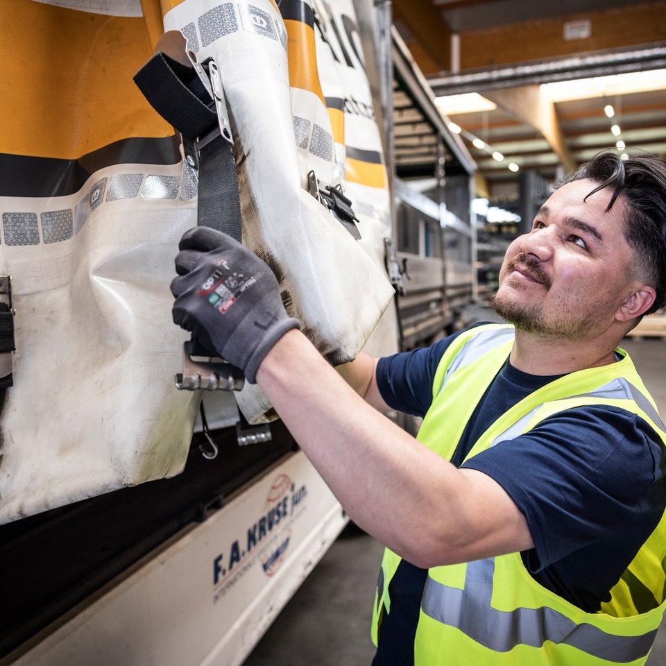 Mitarbeiter in Warnweste öffnet die Seitenplane eines Lkw im Lagerbereich