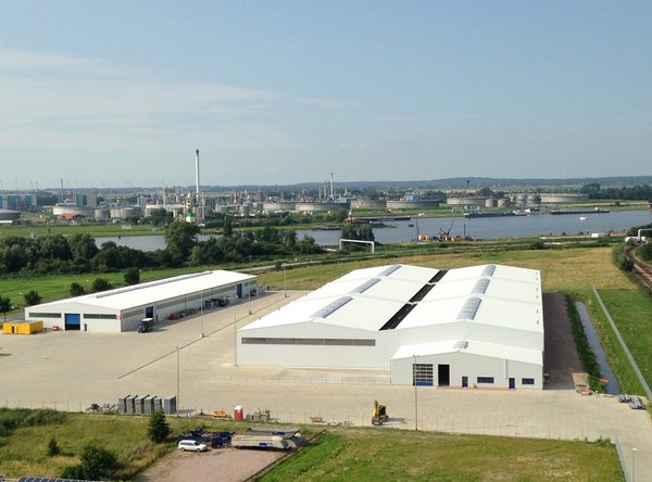 Luftaufnahme eines modernen Lager- und Logistikgeländes mit weißen Hallen und Blick auf einen Fluss.