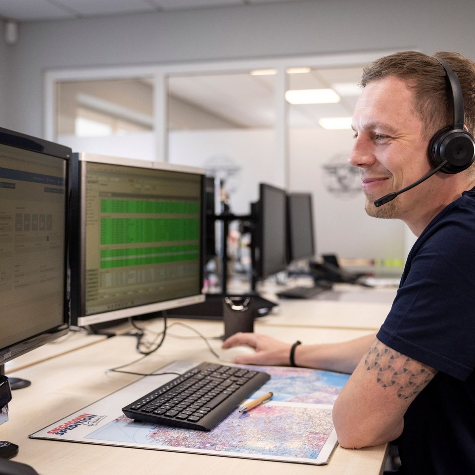 Mitarbeiter mit Headset arbeitet lächelnd an zwei Monitoren in einem modernen Büro
