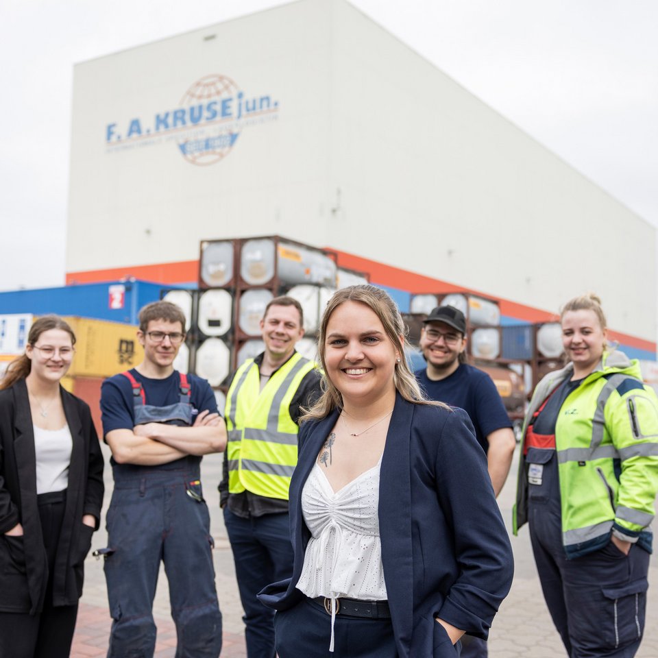 Gruppe von sechs Mitarbeitenden steht vor einer großen Lagerhalle.