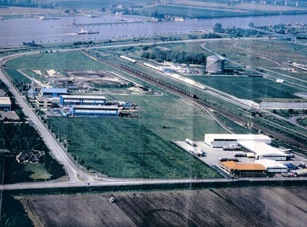 Luftaufnahme eines weitläufigen Industrie- und Logistikgeländes mit Hallen, Straßen und Fluss im Hintergrund.