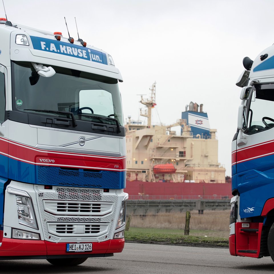 Zwei Lkw der Spedition Kruse frontal gegenüber, im Hintergrund Industrieanlage mit Tanks
