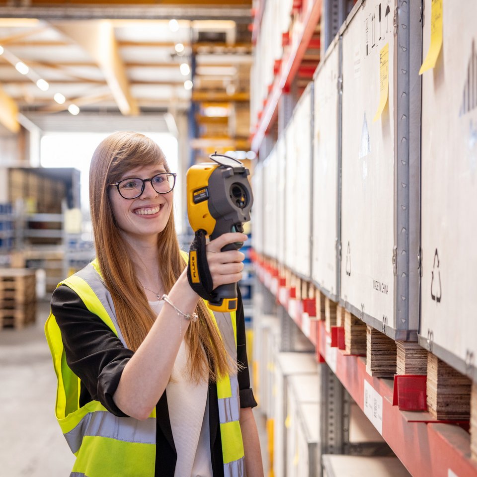 Mitarbeiterin von F.A. Kruse jun. scannt Lagerware mit Handscanner zwischen hohen Regalen.