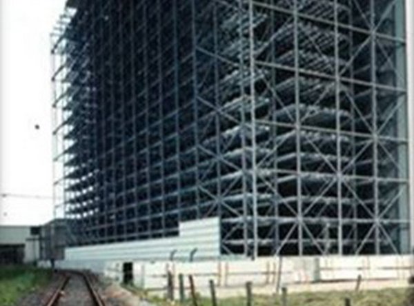 Großes Stahlregallager im Bau neben Bahngleisen auf einer Wiese.