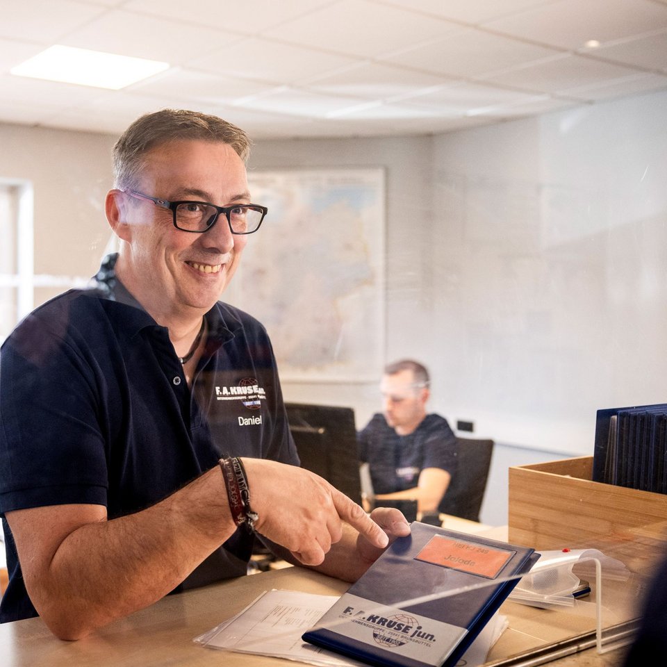 Mitarbeiter steht mit Laptop in den Büroräumlichkeiten von Spedition Kruse und unterhält sich