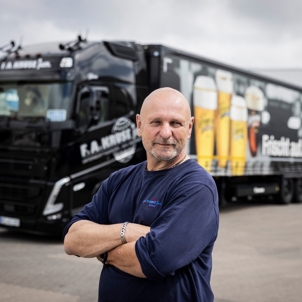 Mann mit verschränkten Armen steht vor einem schwarzen Lkw.