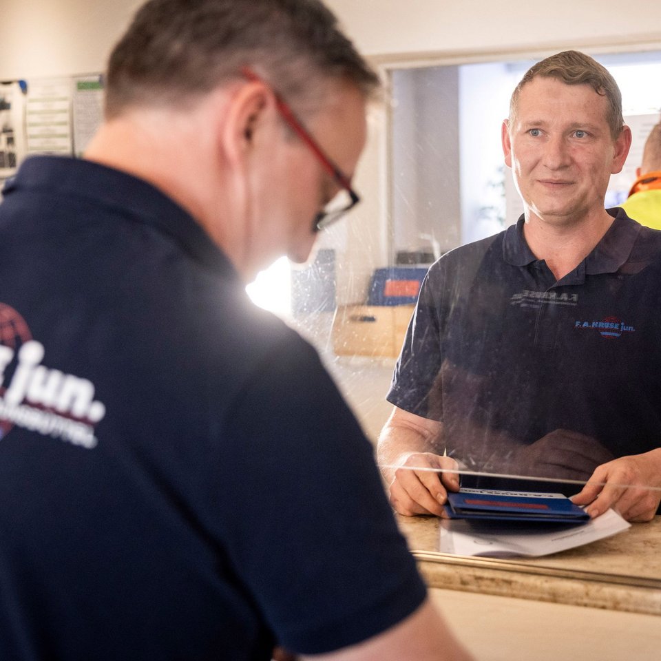 Mitarbeiter der Spedition Kruse bei der Dokumentenübergabe am Schalter mit Plexiglasscheibe