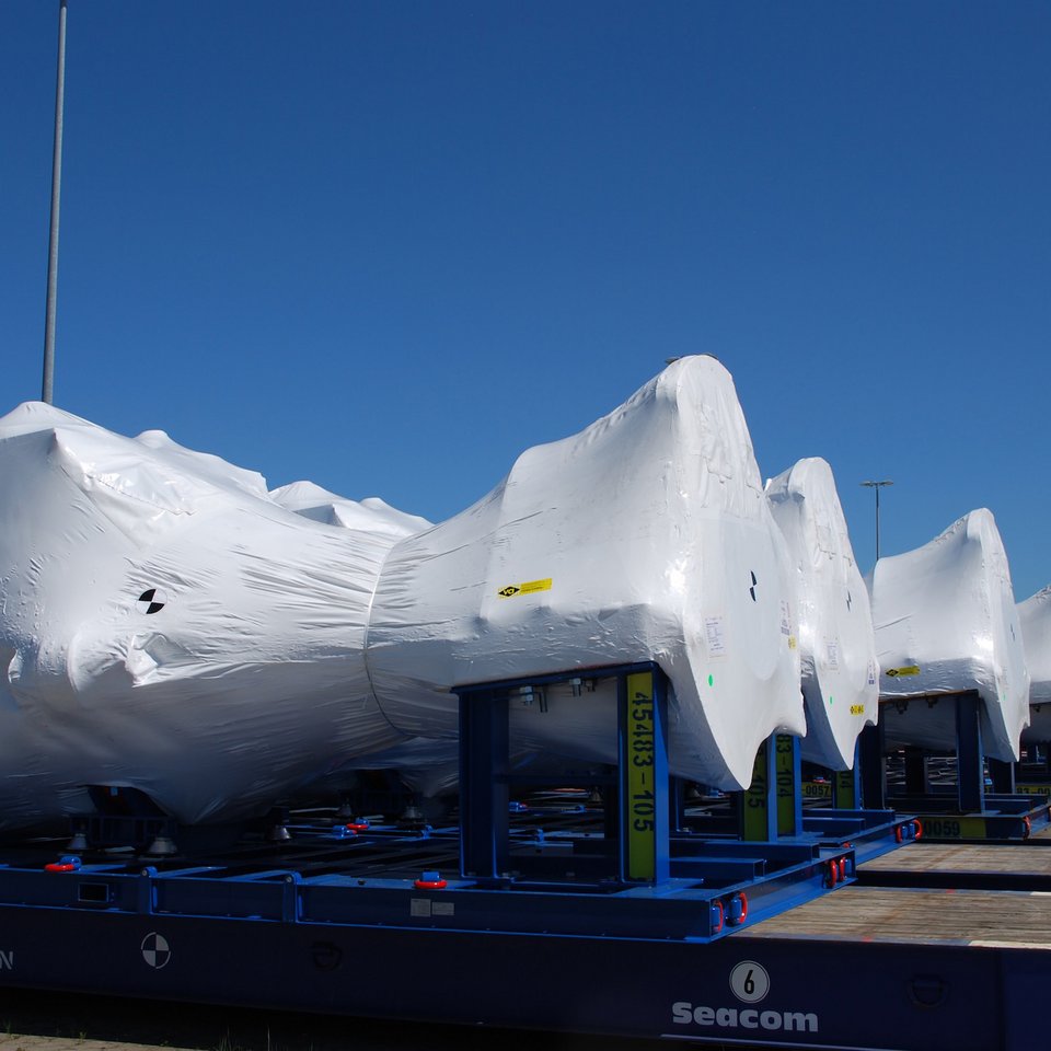 Große Maschinenbauteile in weißer Schutzfolie auf blauen Transportgestellen im Freigelände