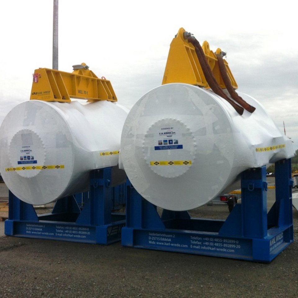 Zwei große Maschinenbauteile in weißer Folie mit gelben Hebevorrichtungen auf blauen Gestellen