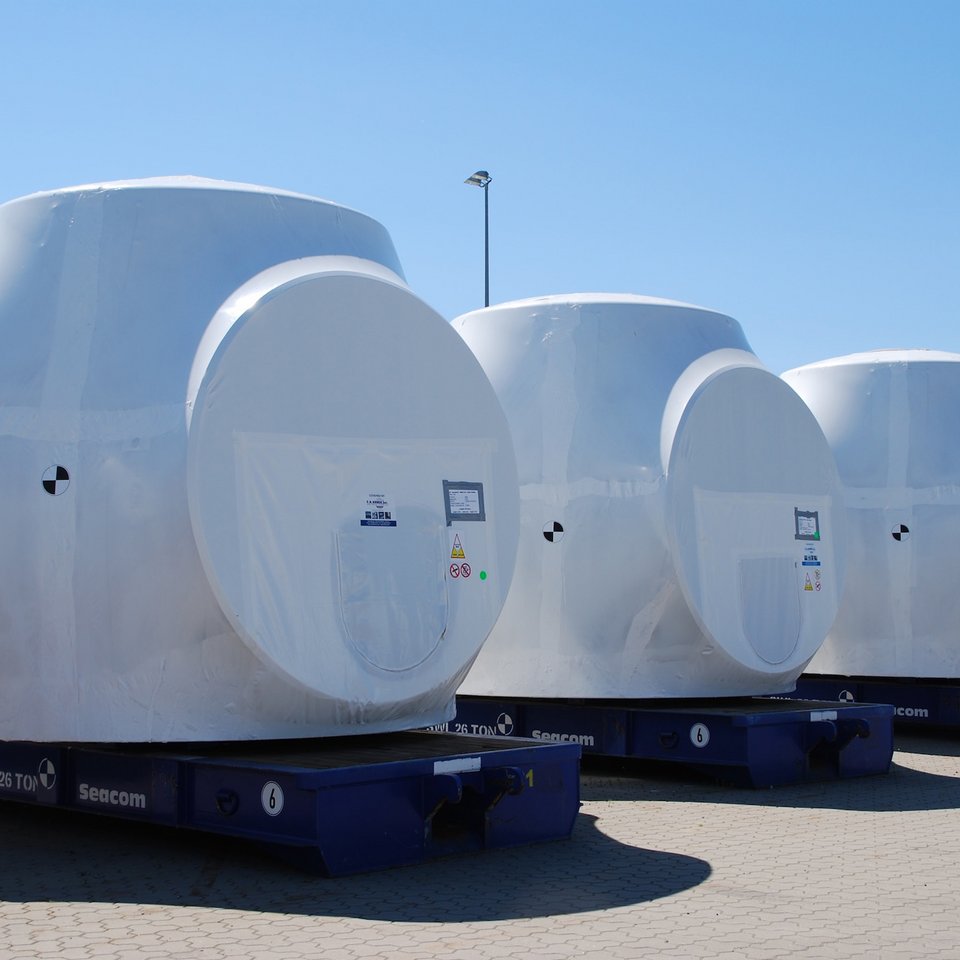 Drei Nacellen von Windkraftanlagen in weißer Schutzfolie auf blauen Plattformen